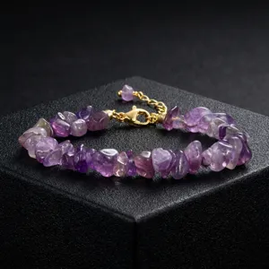 Detailopname van amethist steen armband met onregelmatige paarse stenen en gouden slot.