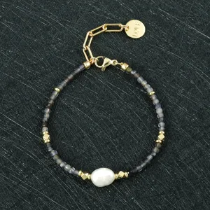 Gedetailleerd close-up van de donkere kralenarmband met barokparel en gouden bedel.