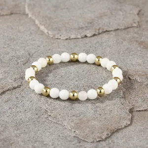 Close-up detail van de minimalistische elastische armband met witte en gouden kralen.