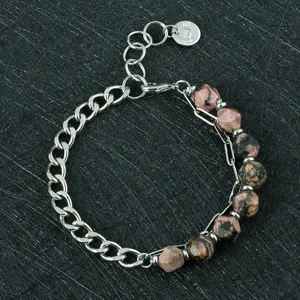 Detailopname van de metalen ketting en gefacetteerde roze edelsteenarmband met liefdeslabel.