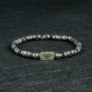 Detailweergave van de 4mm kraal armband met metalen rechthoekige hanger op donkere stenen achtergrond.