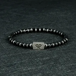 Gedetailleerde close-up van heren zwarte kralenarmband met zilveren metalen accenten en middenhanger.