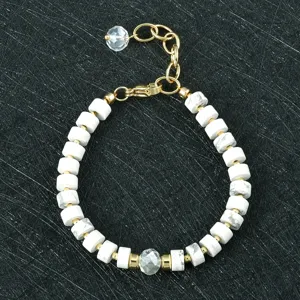 Detailopname van witte stenen kralenarmband met goudkleurige metalen accenten en kristalhanger.