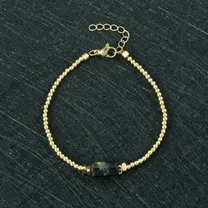 Gold-toned beaded bracelet detail featuring a dark natural stone charm and adjustable chain.