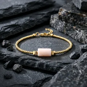 Close-up detail of gold beaded bracelet featuring a pink stone centerpiece on dark slate.