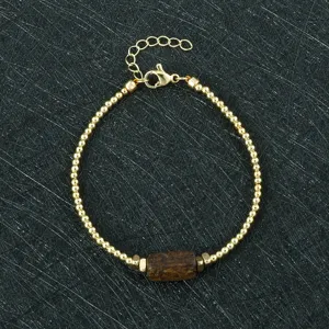 Detail shot of gold-toned beaded bracelet featuring a central dark barrel bead and clasp.