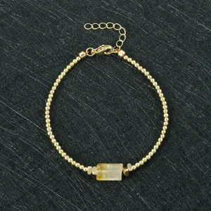 Detail view of golden beaded bracelet featuring an irregular yellow crystal stone charm.
