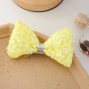 Détail de pince à cheveux nœud à paillettes jaunes, accessoire mignon et scintillant.