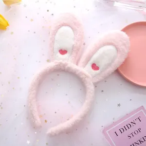Detailed shot of the pink plush bunny ear headband with heart embroidery and soft mesh background.