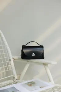 Detalle de bolso bandolera de cuero negro, elegante bolso de mano con asa superior.