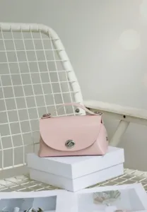 Bolso cruzado de cuero rosa elegante con cierre de giro metálico y diseño moderno.