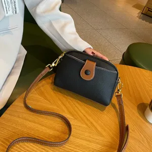 Close-up detail of black leather crossbody bag with brown strap and golden hardware.