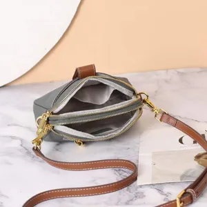Detailed view of genuine leather crossbody bag with dual zipper compartments and strap.