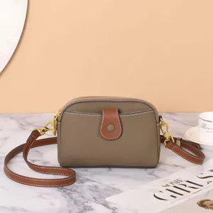 Close-up detail of khaki leather crossbody bag with brown strap and metal hardware.