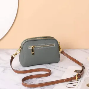 Detailed close-up view of elegant grey leather crossbody bag with brown strap and gold hardware.