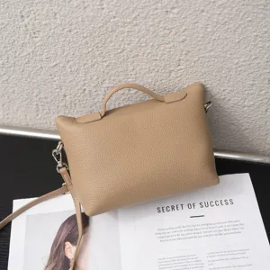 Detalle de un elegante bolso de mano de cuero beige con asa superior y correa ajustable.