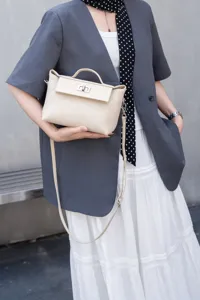 Detalle del elegante bolso cruzado de cuero beige con asa superior y cierre de metal.