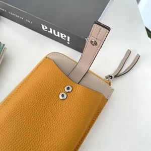 Vista dettagliata della mini borsa telefono in pelle gialla e beige con bottone a pressione e zip.