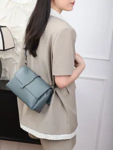 Detail shot of blue-grey leather shoulder bag featuring signature metal bar closure design.