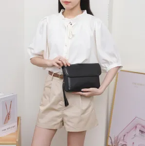 Detailed view of a minimalist black leather clutch bag held by a model, showing fine texture.