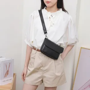 Detailed view of a woman wearing a black leather crossbody waist bag, indoor scene shot.
