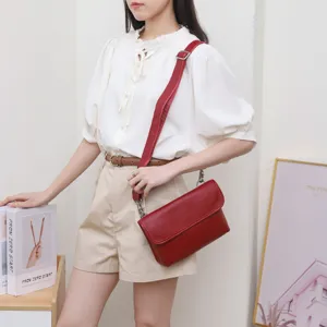 Red leather crossbody bag detail view, showing fine texture, adjustable strap and metal hardware.