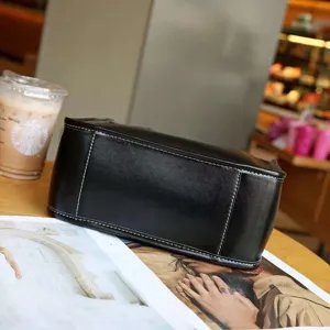 Nahaufnahme der schwarzen Ledertasche mit sauberen weißen Nähten und edler Oberflächentextur.