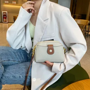 Detail view of casual genuine leather crossbody bag in beige with brown buckle accent.