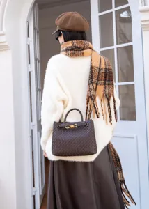 Dettaglio della borsa in pelle intrecciata, tote marrone scuro con nodo in metallo, elegante accessorio.