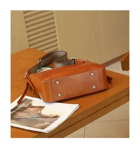 Detail view of vintage brown leather crossbody shoulder bag with metal feet and woven strap.