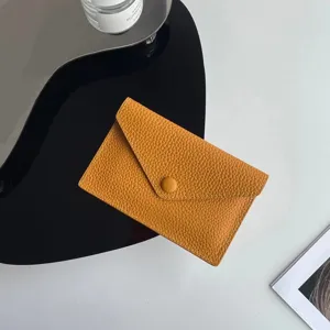 Gros plan détaillé du porte-monnaie en cuir jaune avec texture fine et bouton pression.