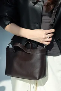 Close-up detail view of dark brown leather handbag, showing fine texture and durable hardware.