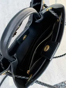 Elegante borsa a secchiello nera intrecciata con manici e dettagli di cinturini intrecciati.