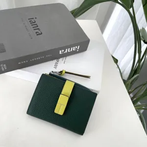 Detail view of dark green leather short wallet with contrast yellow strap, zipper pocket.