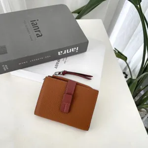 Detailed close-up of brown genuine leather bifold wallet with contrast red strap clasp and fine texture.