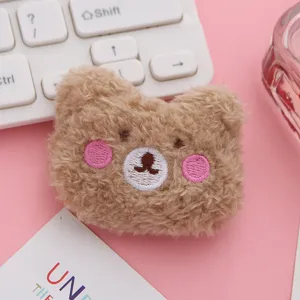 Close-up detail of cute brown plush bear brooch with pink blush and embroidered face.