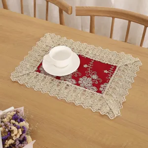 Detail van een rode rechthoekige placemat met elegante gouden borduurwerk en kanten rand.