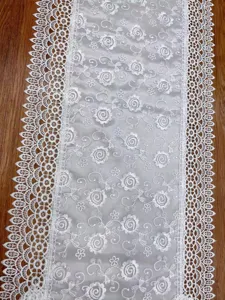 Gedetailleerd overzicht van een elegante witte kanten geborduurde tafelloper voor thuis.