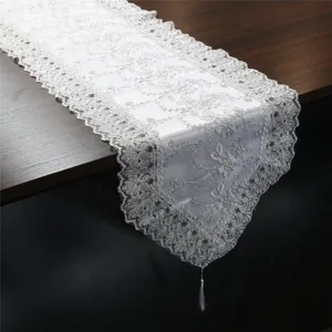Primer plano detallado de camino de mesa de encaje blanco con elegante bordado de plata y borla.