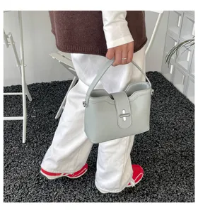 Vue détaillée d'un sac seau chic en cuir grainé gris clair tenu élégamment à la main.