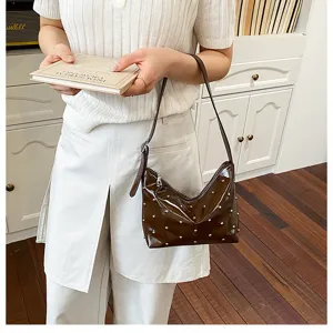 Detailed view of brown patent leather shoulder bag with metallic rivet embellishments.