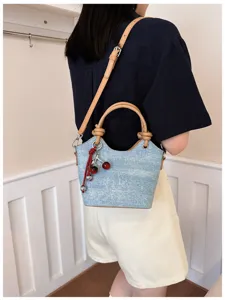 Chic denim bucket bag detail showcasing premium leather handles and cute red cherry charm pendant.