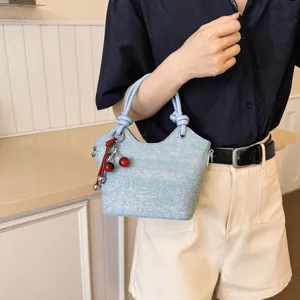 Casual light blue denim bucket bag with knotted handles and cherry charm for daily commute.