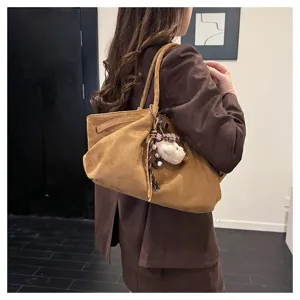 Detail shot of brown suede tote bag worn on shoulder with cute plush charm accessory.