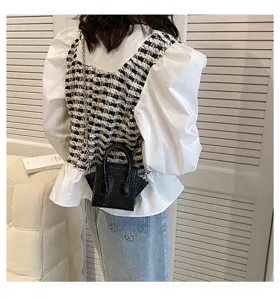 Detail view of a black mini structured handbag with top handles and chain strap in a room.