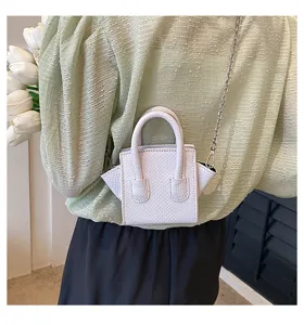 Detail shot of a chic mini white crossbody bag with metal chain and stylish top handles.