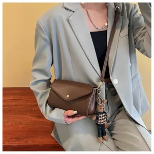 Close-up detail of stylish brown cross-body bag with cute keychain, premium leather texture.