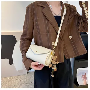 Detailed close-up of a stylish white cylinder crossbody shoulder bag with cute bunny keychain.