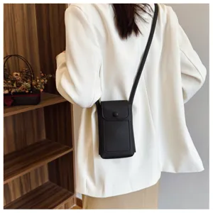 Detail shot of the black soft leather crossbody phone bag worn by a model against wooden decor.