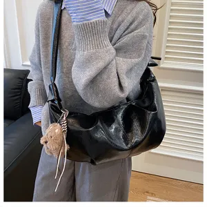 Stylish black shiny slouchy shoulder bag with cute plush keychain, perfect casual daily use.